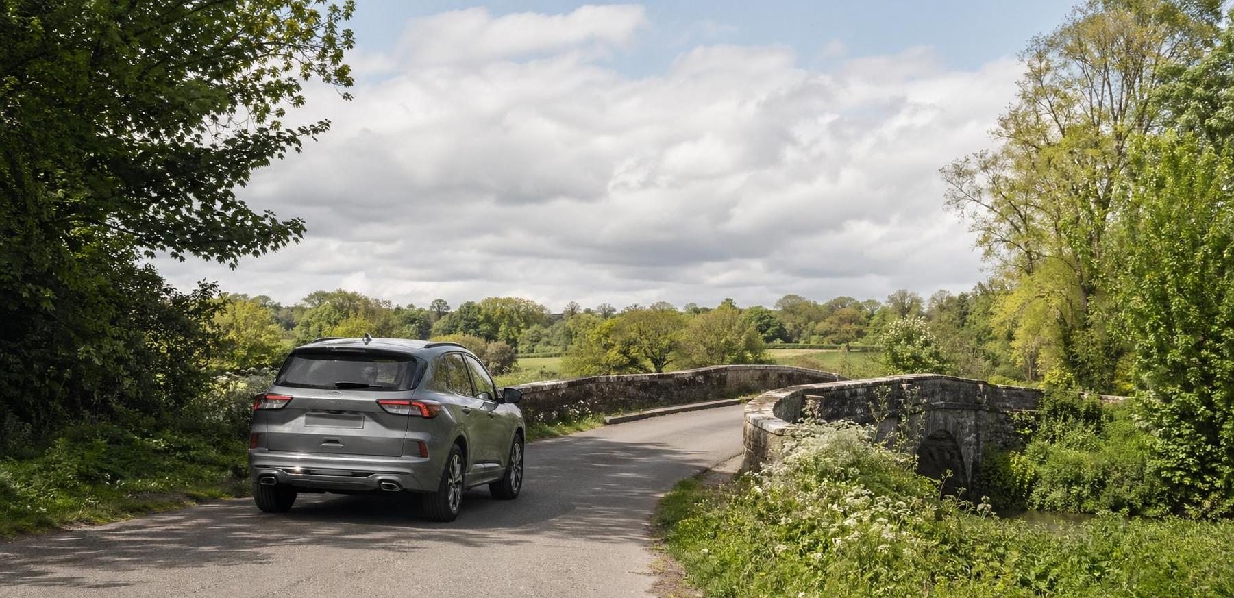 Grey crossover approaching a small stone bridge on a rural road near Crewkerne